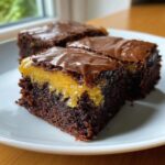 Close-up of fudgy lemon brownies showing a bright yellow lemon curd layer and shiny chocolate topping.