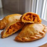 Close-up of golden baked pumpkin empanadas, one cut open revealing the bright orange pumpkin filling.