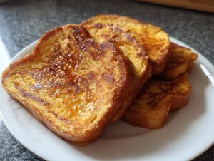 Four golden-brown slices of easy french toast stacked slightly on a white plate, drizzled with syrup.