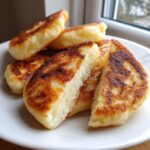Close-up of fluffy, golden-brown Irish potato farls stacked on a white plate, one cut open.