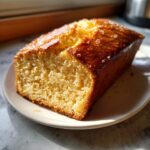A golden brown loaf of freshly baked beer bread with a shiny, slightly crystallized top, resting on a white plate.