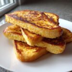 A stack of perfectly golden brown, thick-cut easy french toast slices piled on a white plate.
