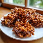 A plate of rich, chocolate-coated haystack cookies made with chow mein noodles, glistening under natural light.