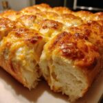 Close-up of cheesy Hawaiian roll garlic bread, showing a section pulled apart revealing soft interior and melted cheddar.