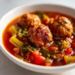 Close-up of a white bowl filled with rich tomato broth, featuring three browned meatballs in this delicious albondigas soup.