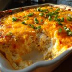 Close-up of a baked hot crab dip in a white dish, showing a scoop removed to reveal shredded crab meat and a melted, bubbly cheese topping.