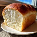 A freshly baked loaf of japanese milk bread, sliced to show its incredibly soft, white, and fluffy interior crumb.