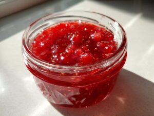 Close-up of a glass jar filled with bright red, chunky freezer jam, showing visible seeds.