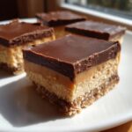 Close-up of a layered no-bake peanut butter bars square with chocolate topping, caramel, and a crumb base.