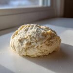A rough ball of pale, slightly crumbly homemade marzipan recipe dough dusted with powdered sugar.