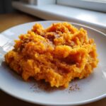 A serving of bright orange mashed sweet potatoes sprinkled generously with cinnamon on a white plate.