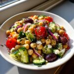 Close-up of a fresh mediterranean chickpea salad featuring chickpeas, cucumber, cherry tomatoes, olives, and feta.