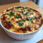 Close-up of a baked Mexican street corn dip in a white bowl, featuring melted, browned cheese and cilantro garnish.