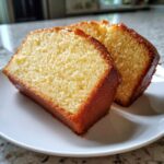 Two thick slices of rich, golden million dollar pound cake served on a white plate.