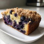 A moist slice of blueberry banana bread topped with brown sugar streusel, served on a white plate.