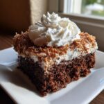 A square slice of moist German chocolate poke cake topped with white frosting, toasted coconut, and a swirl of whipped cream.