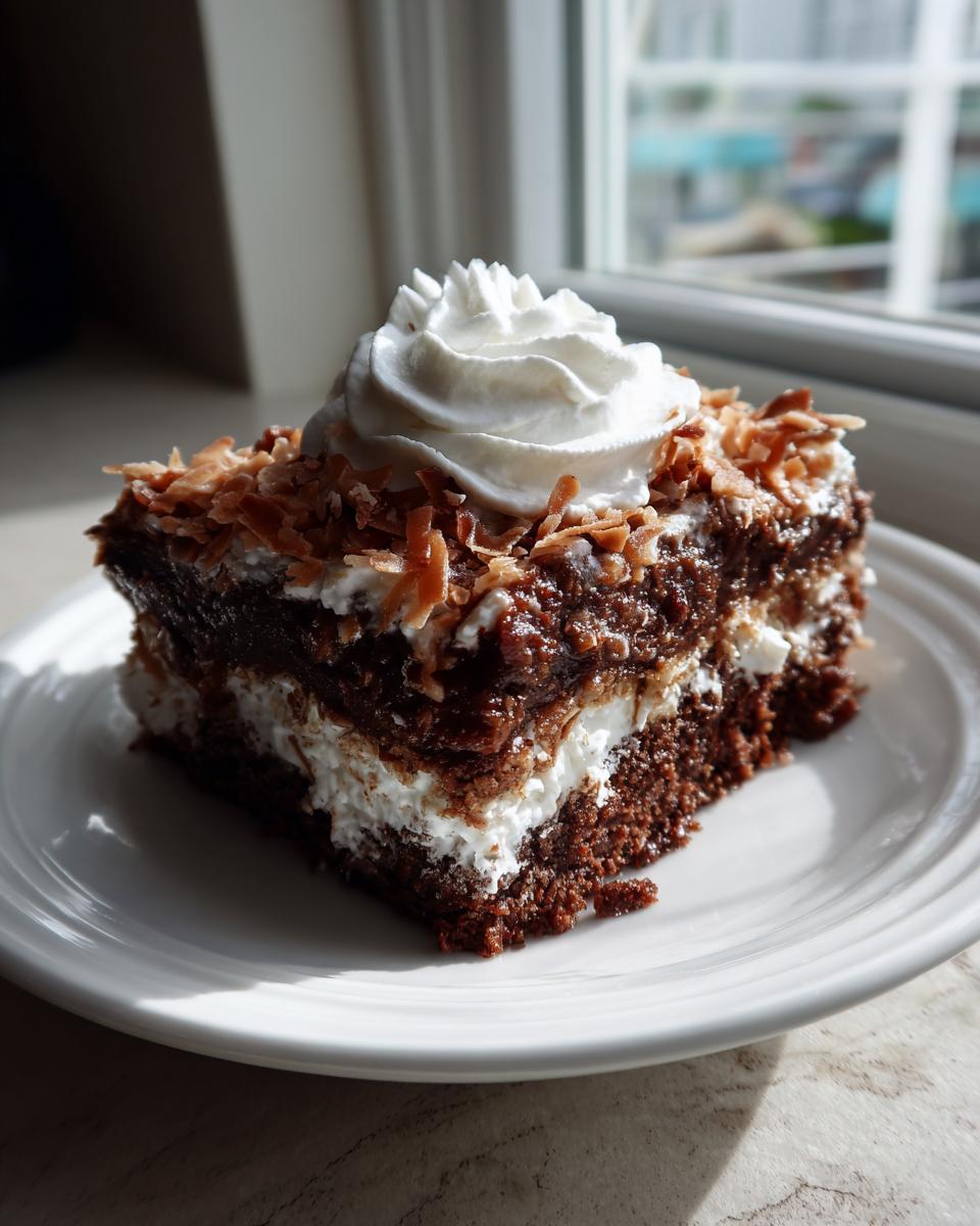 A square slice of moist German Chocolate Poke Cake topped with whipped cream and toasted coconut flakes.