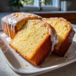 Close-up of a moist lemon loaf, sliced to show the yellow crumb and drizzled with white lemon glaze.