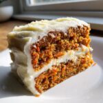 Close-up of a moist slice of carrot cake recipe showing layers of spiced cake and thick cream cheese frosting.