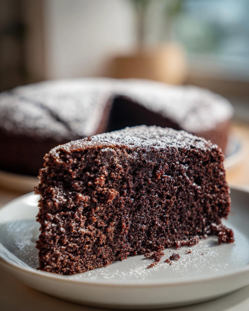 Close-up of a rich, dark slice of gingerbread cake dusted with powdered sugar on a plate.