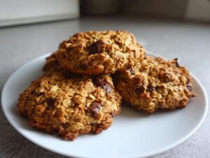 A stack of three hearty, oatmeal chocolate chip breakfast cookie on a white plate.