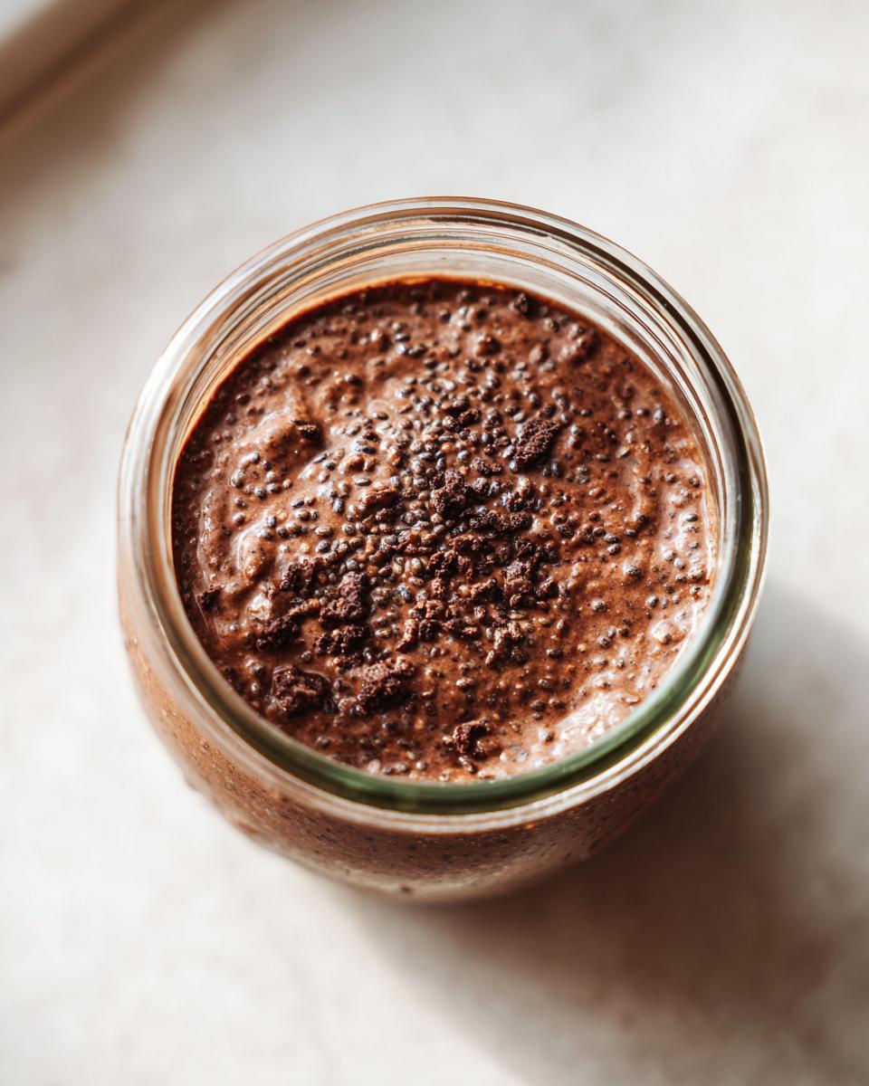 Overhead close-up of rich chocolate overnight oats topped with cocoa powder in a glass jar.