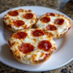 Close-up of three freshly baked pepperoni english muffin pizza halves topped with melted, bubbly cheese.