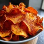 Close-up of a bowl piled high with crispy, orange sweet potato chips seasoned with spices.