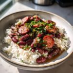 A close-up of a bowl of savory red beans and rice topped with sliced sausage and fresh parsley.
