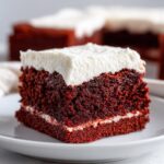 A close-up of a rich, dark red velvet brownies square topped with thick white cream cheese frosting.