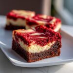 A decadent square of red velvet cheesecake brownies showing distinct brownie, cheesecake, and swirled red velvet layers.