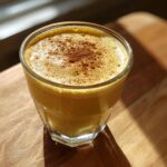 A glass of rich, yellow homemade eggnog topped with a dusting of cinnamon spice.