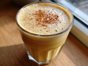 Close-up of rich homemade eggnog in a glass, topped with frothy foam and a dusting of cinnamon.