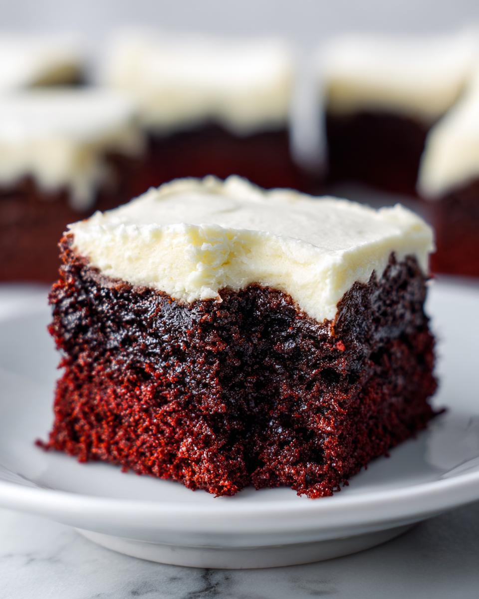 A moist, dark red square of red velvet brownies topped with thick cream cheese frosting.