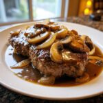 A close-up of rich Salisbury steak smothered in brown gravy, sautéed mushrooms, and onions.