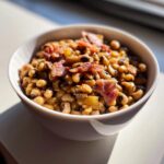 Close-up of a white bowl filled with savory black eyed peas topped with crispy bacon pieces.