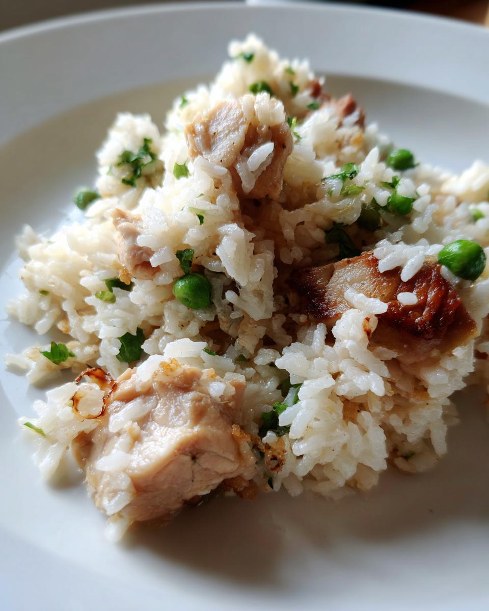 Close-up of a serving of fluffy white rice mixed with chunks of chicken, green peas, and parsley, representing one pot chicken and rice.