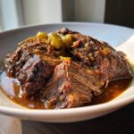 Close-up of tender, shredded Mississippi Pot Roast served in a white bowl with rich brown sauce and pepperoncini peppers.