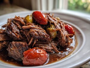 Close-up of tender, shredded Mississippi pot roast served in its rich gravy with whole pepperoncini peppers.
