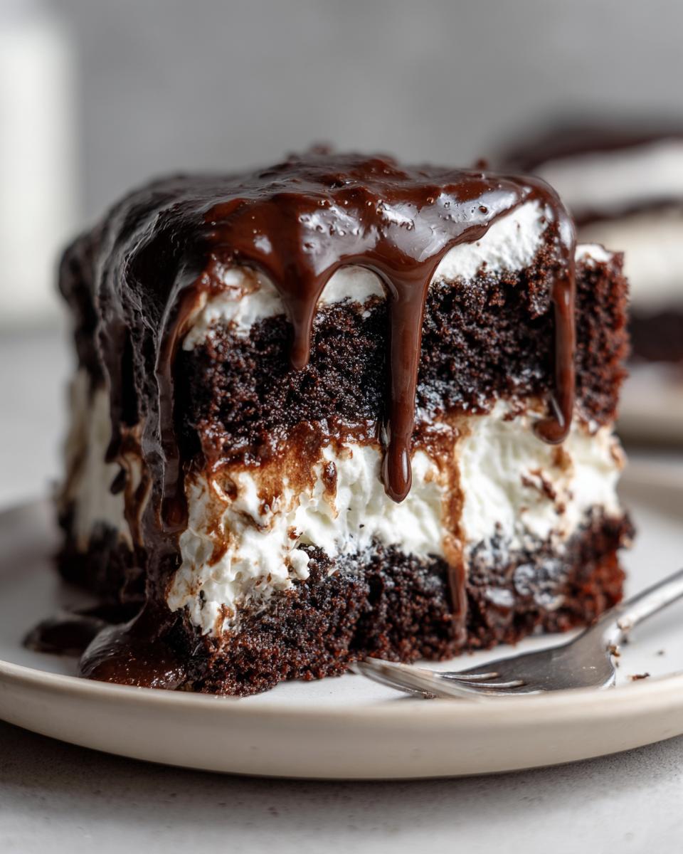 A decadent slice of chocolate poke cake layered with white filling and topped with thick, dripping chocolate fudge sauce.
