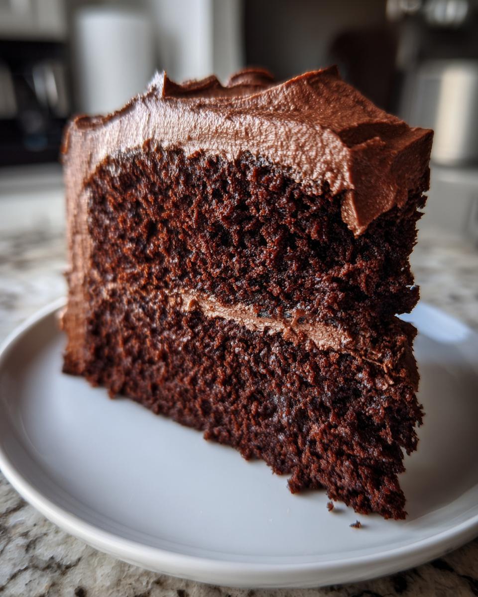 Close-up of a moist slice of homemade chocolate cake layered with thick chocolate frosting.
