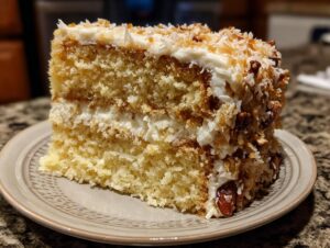 Close-up of a moist slice of white German chocolate cake layered with cream and topped with toasted coconut and pecans.