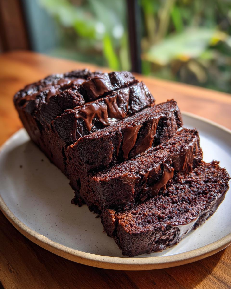 A loaf of rich, dark hot fudge brownie bread, sliced and drizzled with melted chocolate, sitting on a plate.