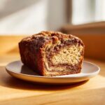 A close-up of a freshly baked snickerdoodle banana bread loaf with a cinnamon swirl, sitting on a small white plate.
