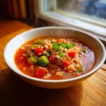 A close-up of a steaming bowl of stuffed pepper soup containing ground meat, rice, and chunks of green and red peppers.