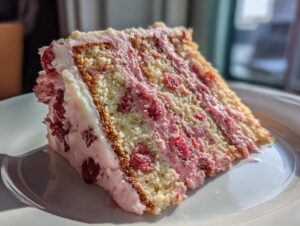 Close-up of a tall slice of strawberry cake showing layers of yellow sponge, pink strawberry filling, and white frosting.