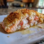A close-up of a perfectly baked stuffed salmon fillet with a golden, crispy breadcrumb topping and rich seafood filling.
