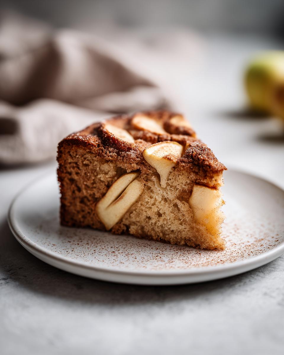 Close-up of a moist slice of Swedish apple cake topped with baked apple slices and sprinkled with cinnamon.