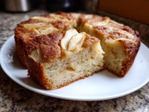 Close-up of a slice cut from a moist Swedish apple cake, showing tender crumb and cinnamon-topped apples.