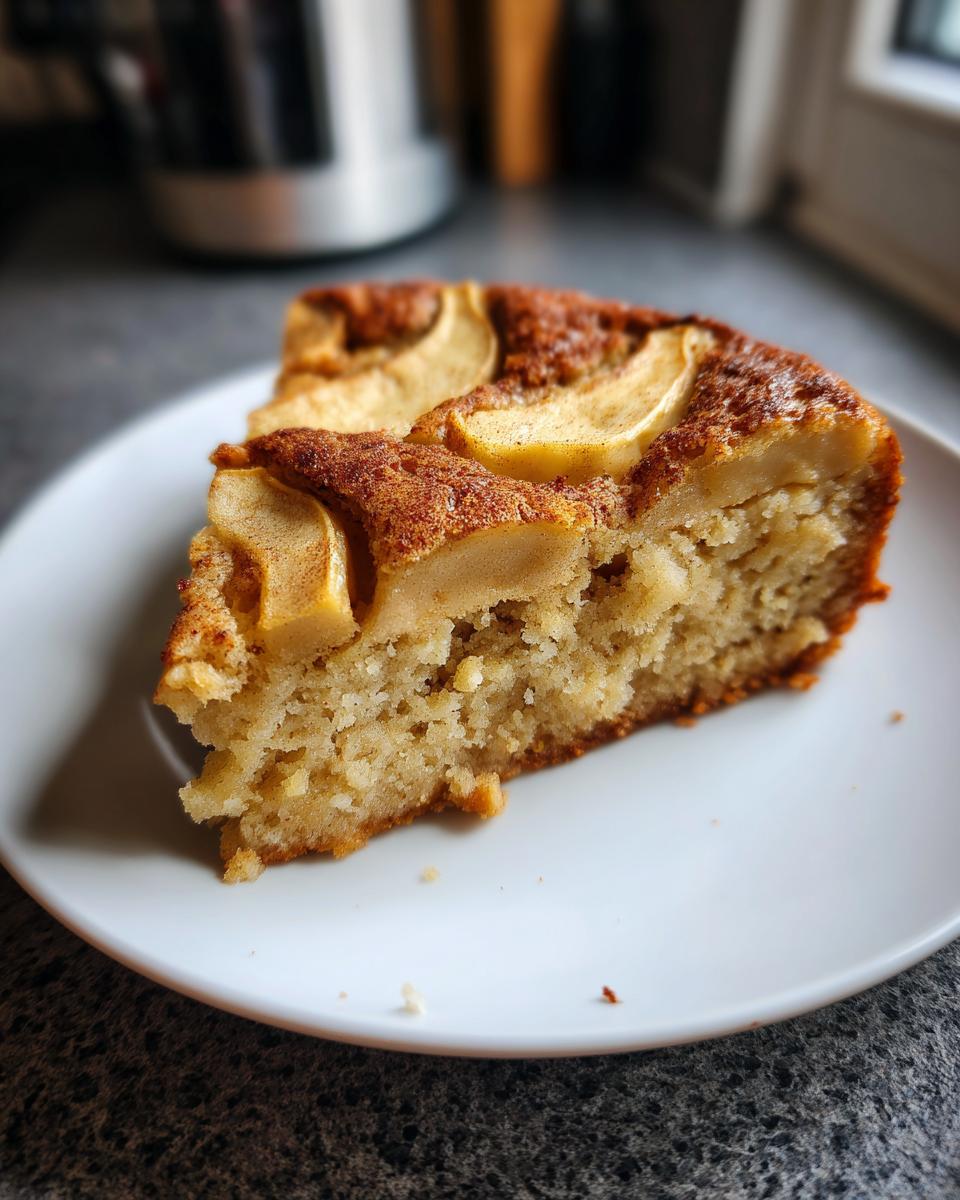 A close-up of a moist slice of Swedish apple cake topped with baked apple slices and cinnamon.